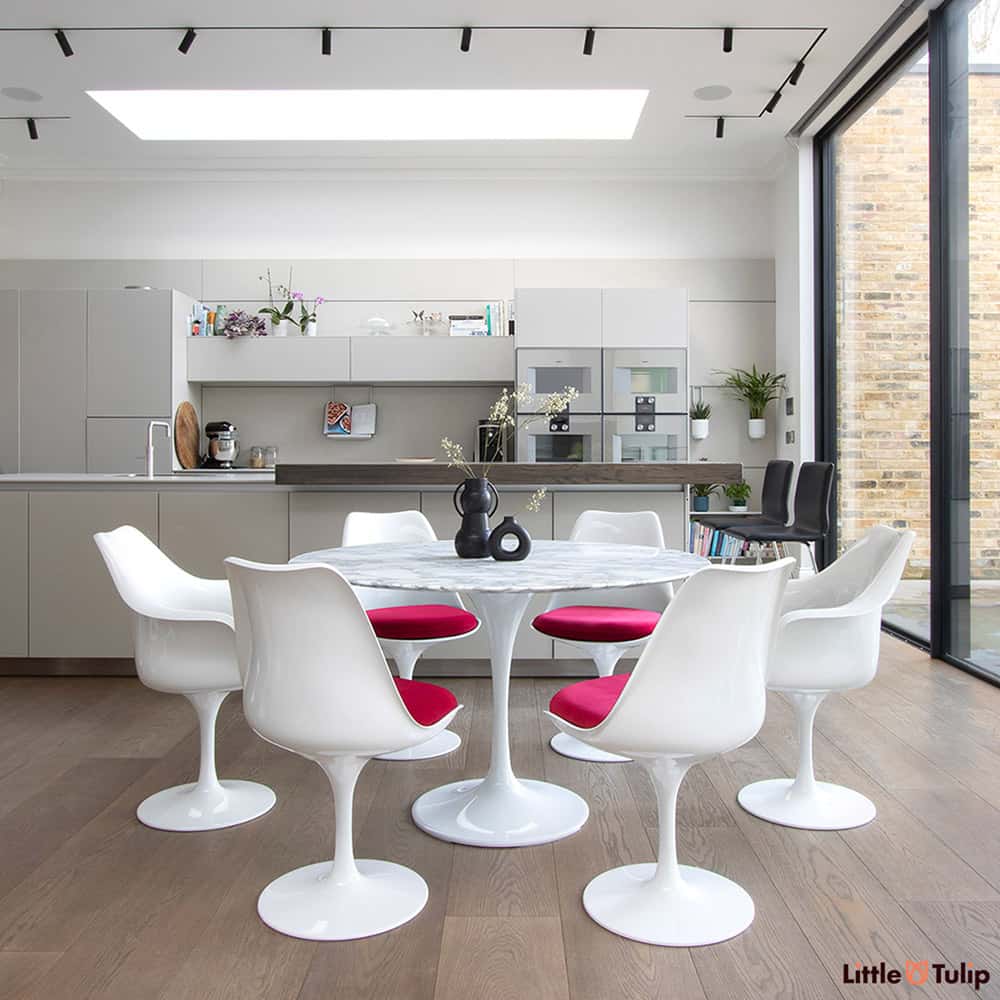 Set within a modern kitchen extension, four tulip side & 2 tulip arm chairs with red pads sit next to the wonderful 120 cm round Arabescato Marble table